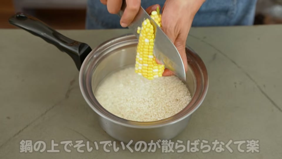 鍋の上でとうもろこしの実を削ぎ落とす
